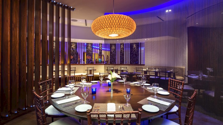 A round dining table set with plates and glasses in an elegant restaurant featuring wooden elements and ambient lighting.