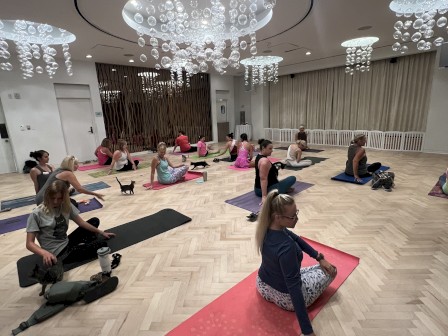 People are practicing yoga on mats in a modern room with elegant chandeliers and wooden flooring, creating a serene atmosphere.