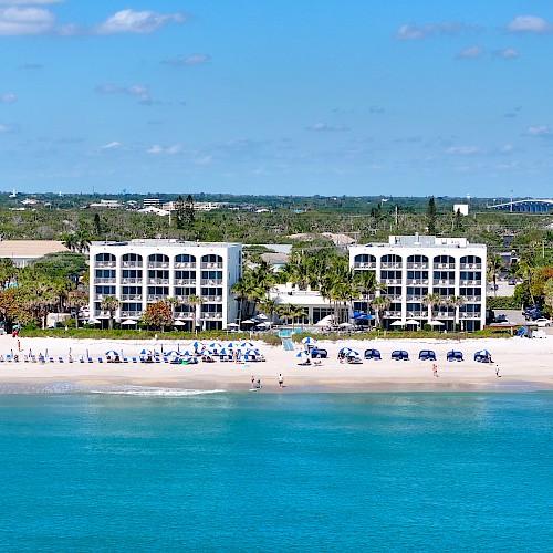 Beachfront view with turquoise water, white sand, and buildings lined along the coast under a clear blue sky.