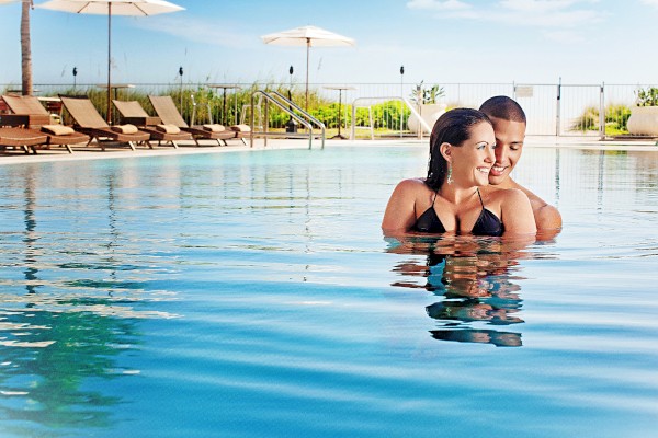 Two women are smiling and enjoying their time together while partially submerged in a swimming pool on a sunny day.