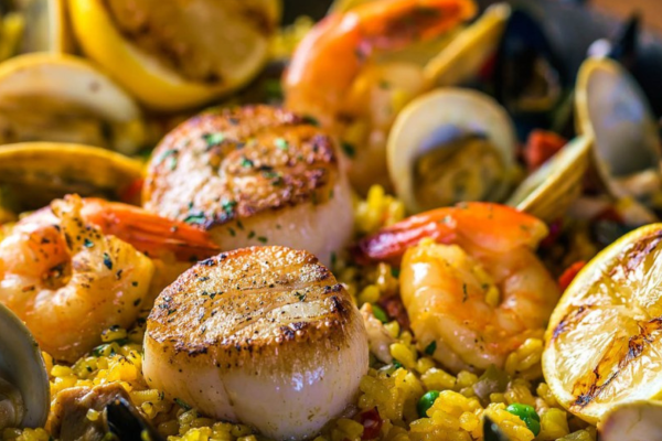 A seafood paella with seared scallops, shrimp, mussels, clams, and lemon slices on a bed of saffron-infused rice.