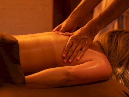 A person is receiving a back massage in a dimly lit room, creating a relaxing and soothing atmosphere.