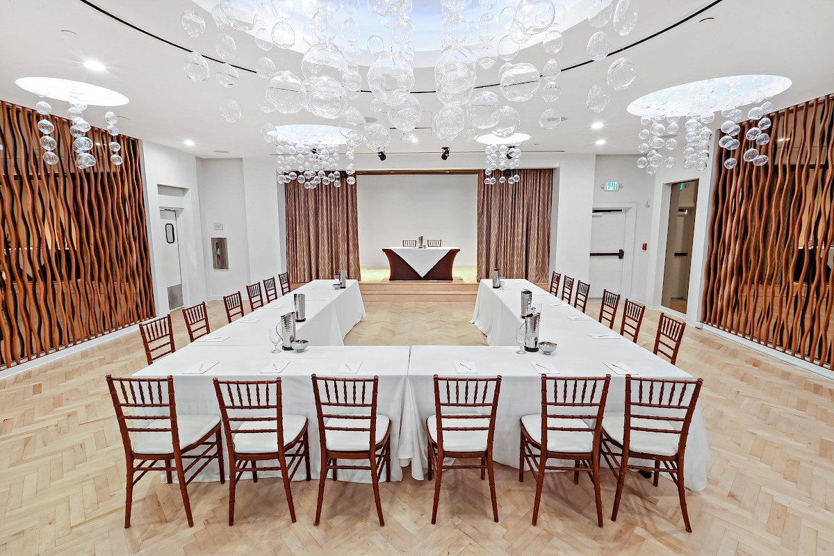 The image shows a conference room set up in a U-shaped table arrangement with chairs, water pitchers, and decorative hanging lights.