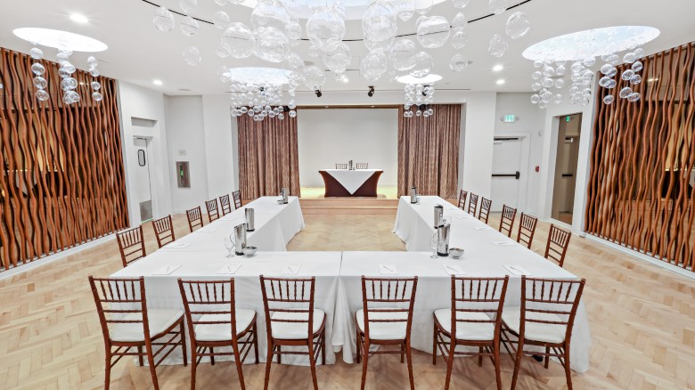 The image shows a conference room set up in a U-shaped table arrangement with chairs, water pitchers, and decorative hanging lights.