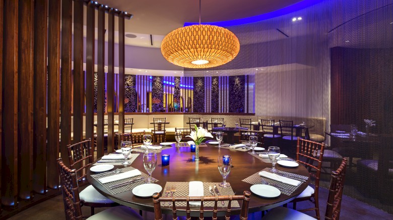 A modern dining room with a large round table set for eight, featuring elegant lighting and decor in a stylish ambiance.
