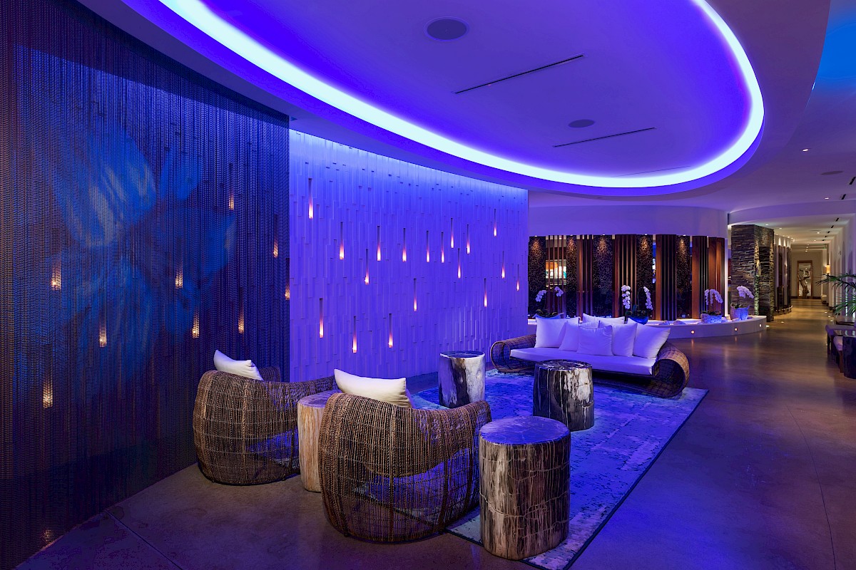 A modern lounge with ambient purple lighting, wicker chairs, and hanging lights, creating a cozy and elegant atmosphere.
