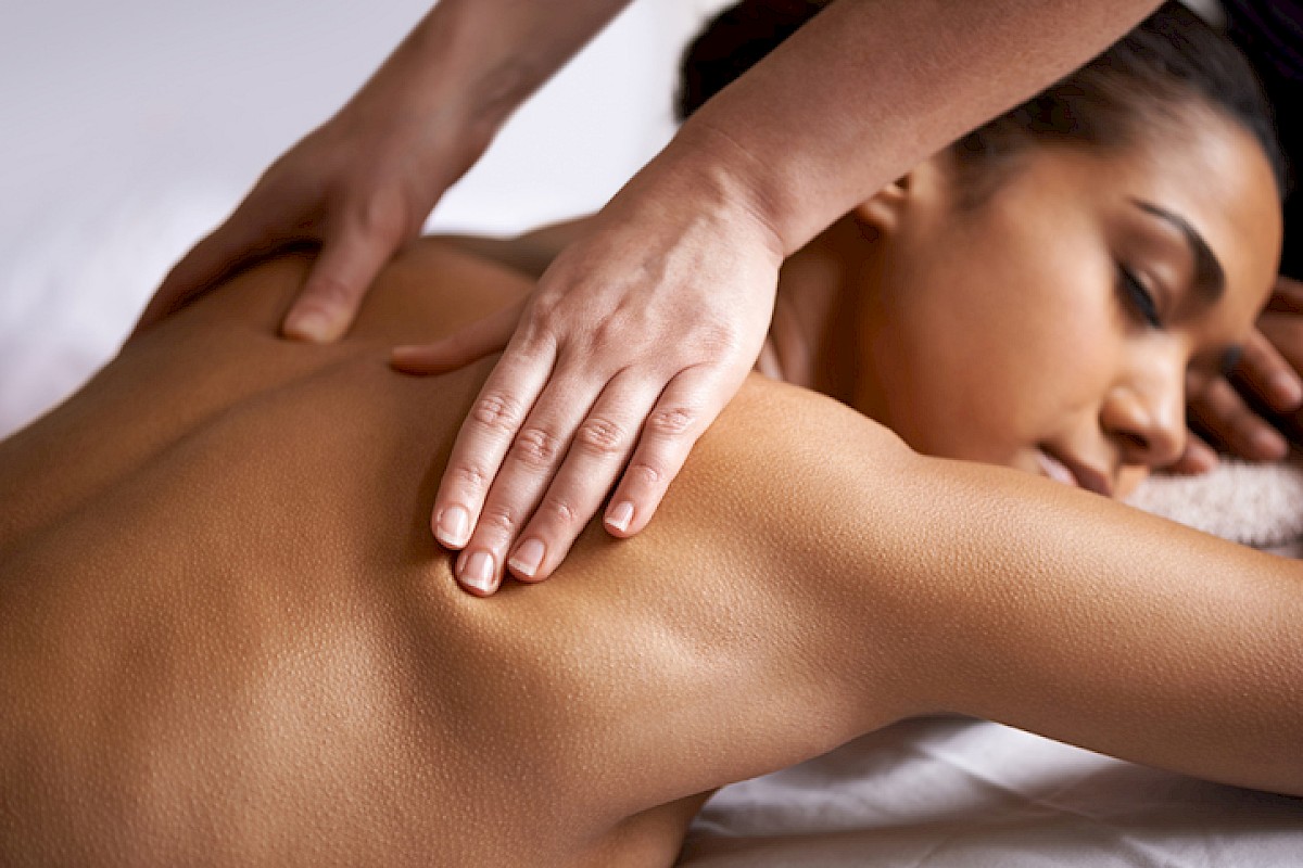 A woman is receiving a back massage from a therapist in a serene setting for relaxation and wellness purposes.