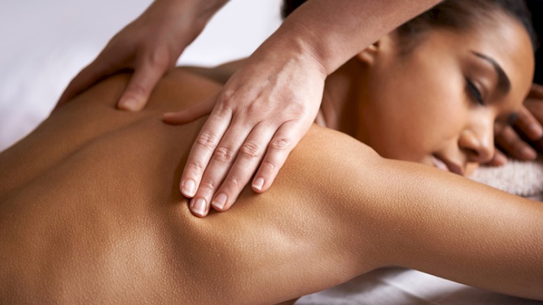 A woman is receiving a back massage from a therapist in a serene setting for relaxation and wellness purposes.