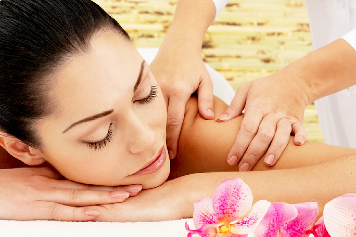 A woman is receiving a shoulder massage at a spa, with pink orchids and a serene background for relaxation.