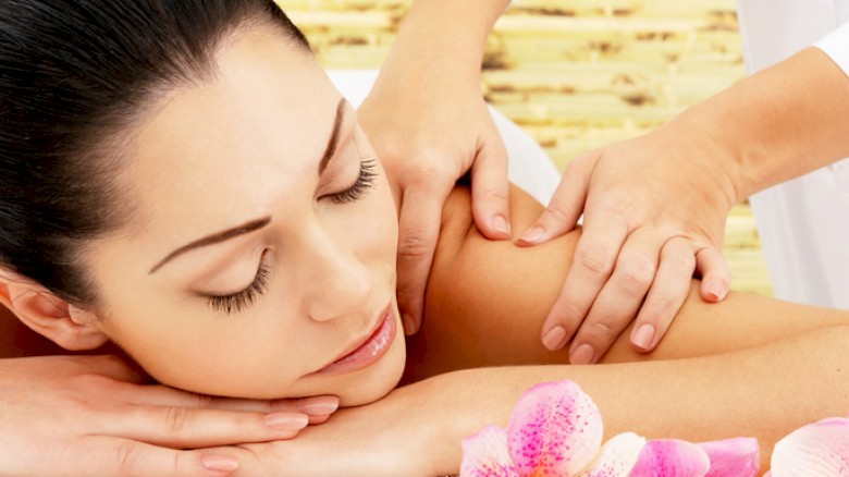A woman is receiving a shoulder massage at a spa, with pink orchids and a serene background for relaxation.