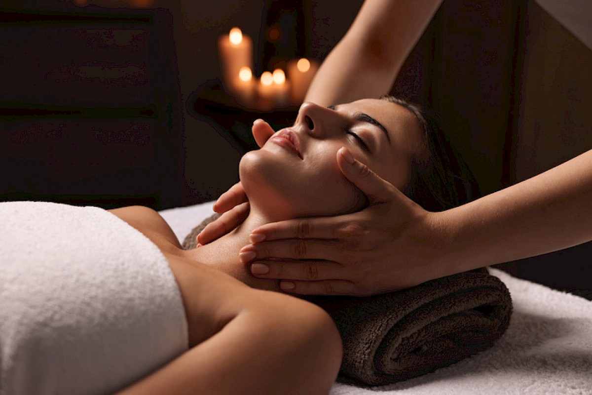 A person receiving a neck massage in a tranquil setting with rolled towel and lit candles in the background for a relaxing ambiance.
