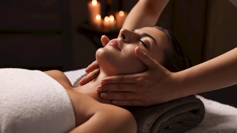 A person receiving a neck massage in a tranquil setting with rolled towel and lit candles in the background for a relaxing ambiance.