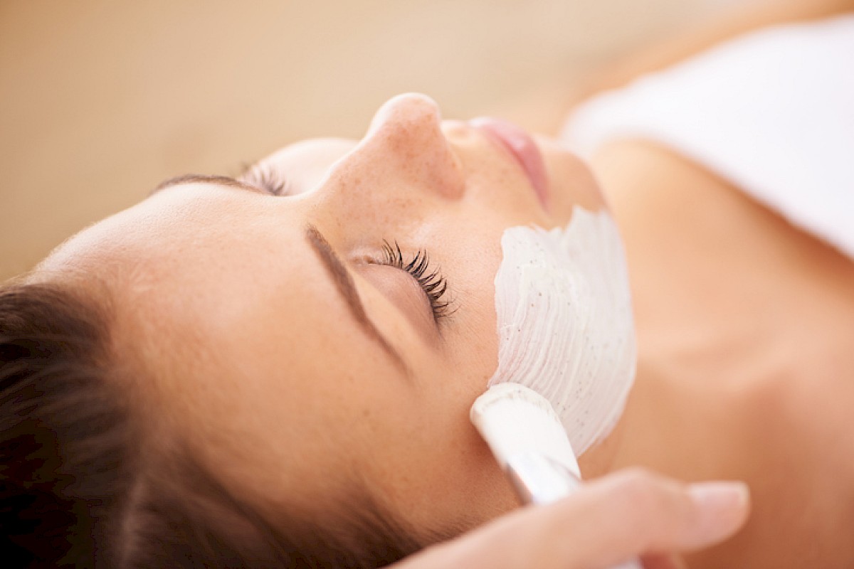 A woman is getting a facial treatment with a mask applied, lying down with eyes closed in a relaxing skincare session.