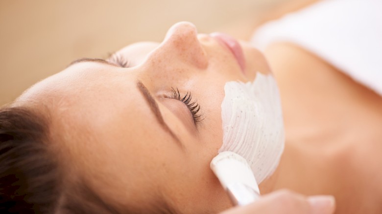 A woman is getting a facial treatment with a mask applied, lying down with eyes closed in a relaxing skincare session.