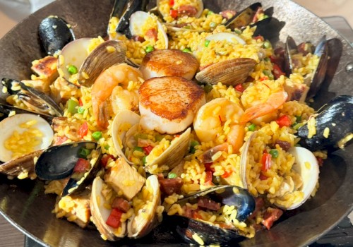 A seafood paella-style dish with mussels, clams, shrimp, scallops, and chunks of fish over saffron rice, colorful vegetables, and herbs.