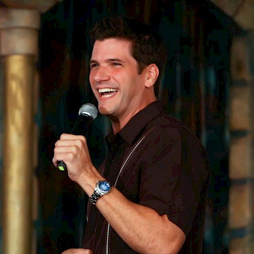 Alex is performing on stage, holding a microphone and smiling.