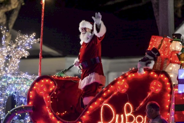 Santa waving from a festive float decorated with lights and gifts during a Christmas parade.