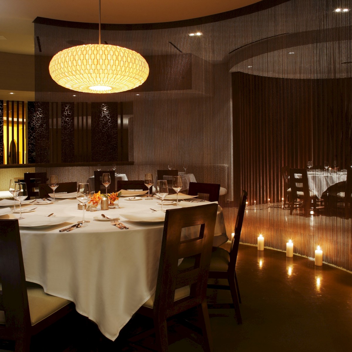 An elegantly set round dining table in a dimly lit restaurant with a chandelier and decorative candles on the floor.