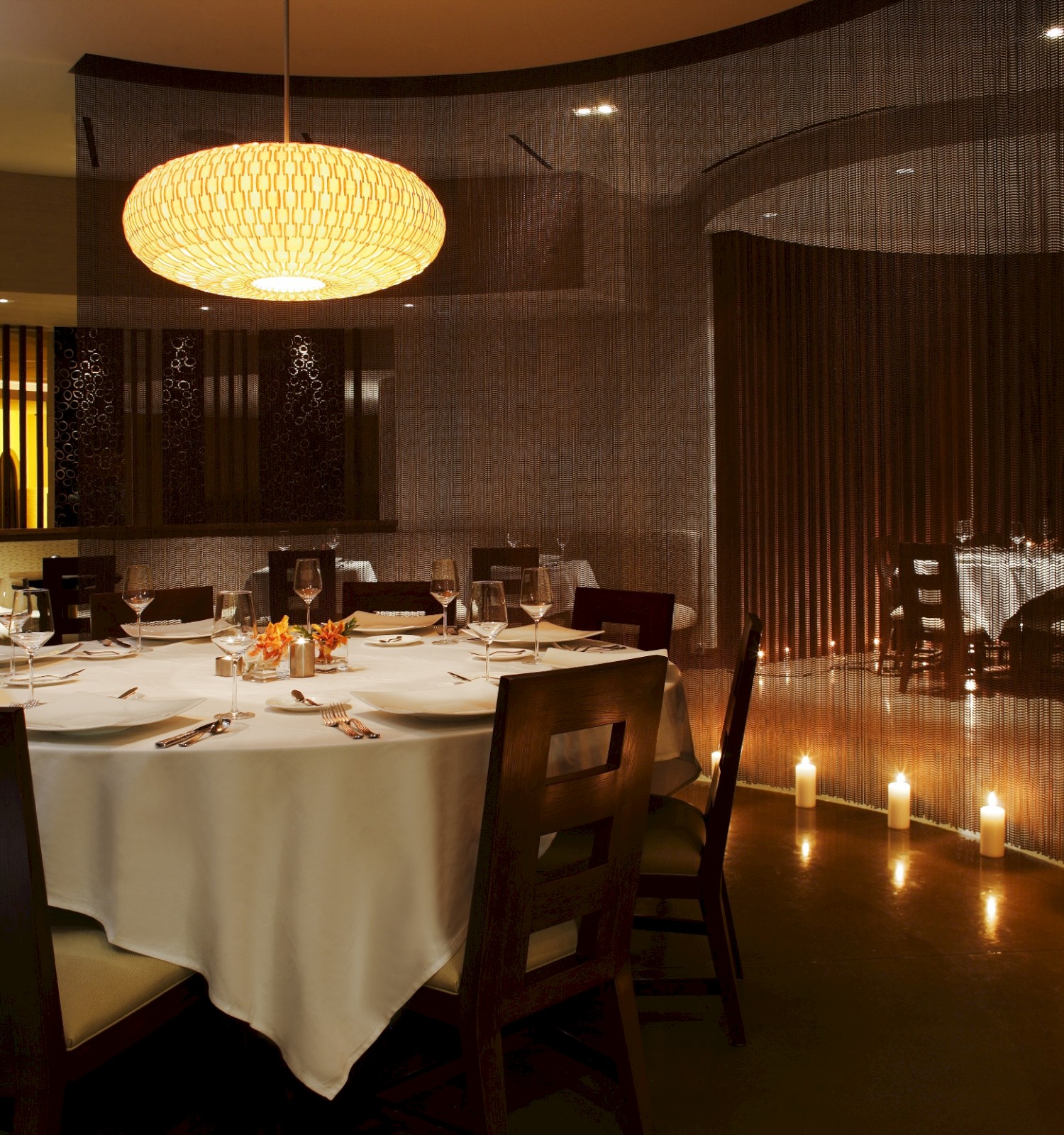 An elegantly set round dining table in a dimly lit restaurant with a chandelier and decorative candles on the floor.