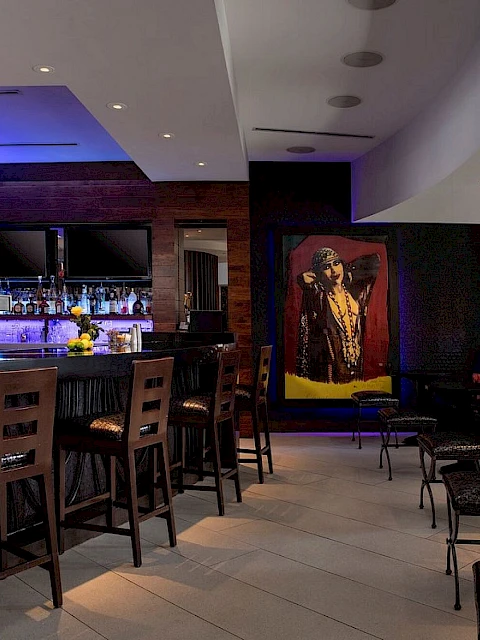 The image shows a stylish bar with high chairs, mood lighting, and wall art, creating a modern, cozy atmosphere.