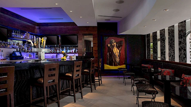 The image shows a stylish bar with high chairs, mood lighting, and wall art, creating a modern, cozy atmosphere.